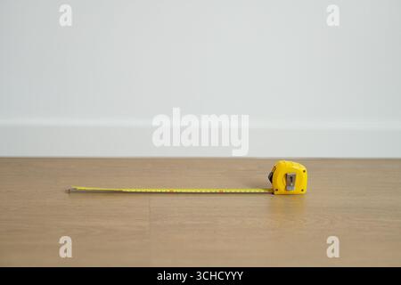 Concepts de remodelage, de déménagement et de plans d'étage, Un ruban à mesurer placé sur un plancher en bois contre un fond de mur blanc Banque D'Images