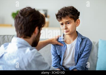 Père et fils triste ayant du cœur à cœur parler à la maison, papa essayant de résoudre des problèmes, parent apaisant garçon Banque D'Images