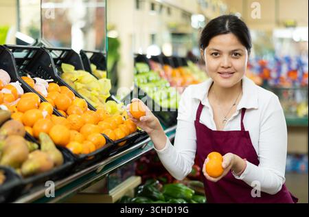 Une jeune femme en uniforme vend des mandarines à l'épicerie Banque D'Images