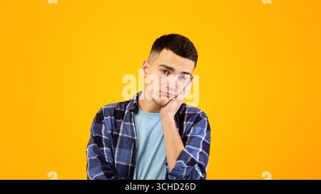 Portrait d'un jeune homme s'ennuiant, se penchant sur sa main, ayant une journée terne sur fond orange studio Banque D'Images