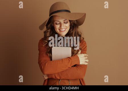 Une femme sereine avec les yeux fermés, exsudant le contentement, embrasse un livre rose à sa poitrine. Habillée à la mode automnale, elle incarne le confort et la joie de Re Banque D'Images