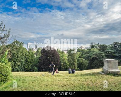 PARIS, FRANCE - 27 JUIN 2025 : les visiteurs se reposent sur une pente herbeuse du Parc des Buttes Chaumont tout en regardant vers le panorama de Paris. Parc des B. Banque D'Images
