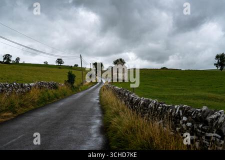 Serpentant le long d'une route asphaltée humide à travers des prairies verdoyantes, mettant en valeur la beauté de la campagne anglaise sous un ciel orageux spectaculaire Banque D'Images