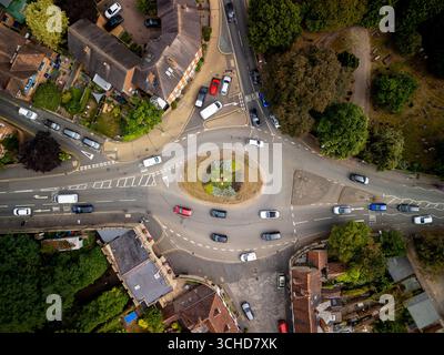 Vue aérienne du trafic circulant autour d'un rond-point dans une petite ville du Royaume-Uni, entourée de maisons, d'arbres et d'un cimetière Banque D'Images