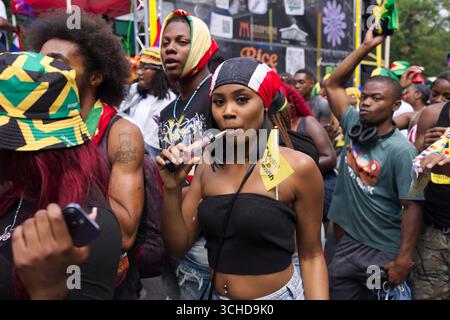 Un groupe diversifié de personnes assiste à un événement extérieur. Une femme au premier plan vape et tient un drapeau jaune. Banque D'Images