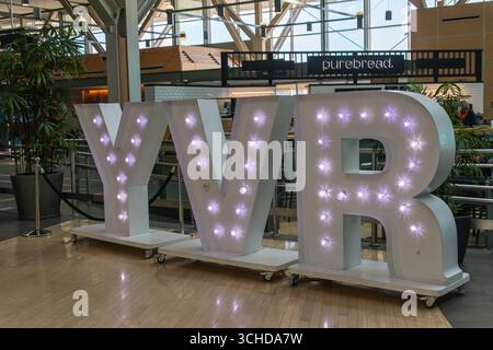 De grandes lettres YVR éclairées sont affichées à l'intérieur de l'aéroport international de Vancouver, près de l'aire de restauration, au décor moderne et à la lumière naturelle. Banque D'Images