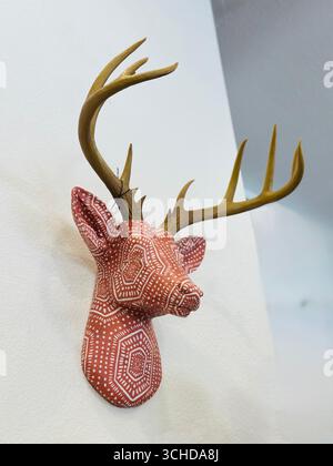 Support mural décoratif fait à la main pour tête de cerf avec motif de points géométriques tribal peint, avec des bois réalistes, affichés sur un mur blanc à l'intérieur. Banque D'Images