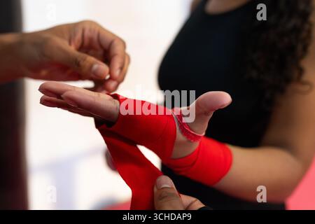 Athlète féminine en haut sans manches noir avec entraîneur masculin enveloppant les mains rouges dans la salle de boxe Banque D'Images