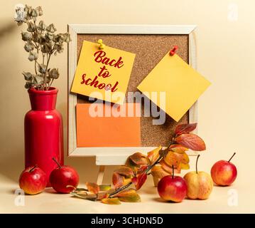 Décor dynamique de la rentrée des classes avec un panneau de liège orné de notes adhésives, vase rouge et pommes fraîches, créant une atmosphère accueillante pour l'éducation Banque D'Images
