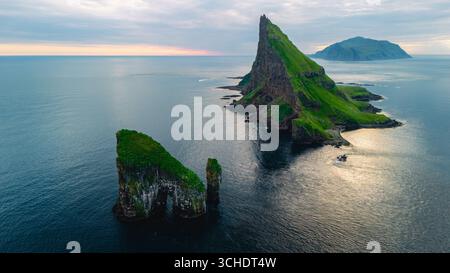 Superbe paysage de falaise de Drangarnir des îles Féroé avec des pics verdoyants s'élevant de la mer, reflétant les douces teintes du lever du soleil illuminant les eaux autour d'imposantes formations rocheuses. Banque D'Images