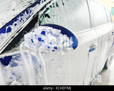 Voiture bleue recouverte de mousse dans un lave-auto en libre-service. Gros plan détaillé, vue grand angle, personne Banque D'Images