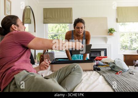 Déballage couple triant vêtements de la valise ouverte sur le lit dans une chambre confortable, affichage de l'écran de tablette Banque D'Images