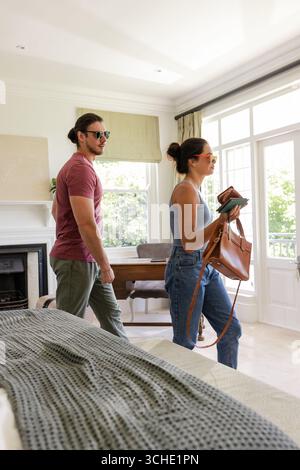 Marchant couple se dirigeant vers les portes françaises dans une chambre lumineuse, portant sac à main et documents de voyage Banque D'Images