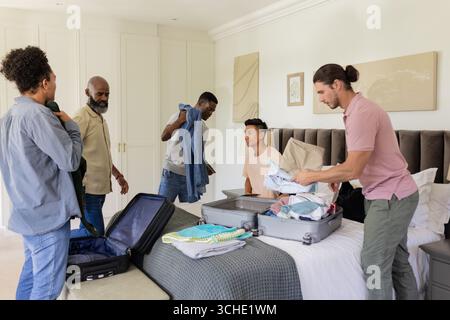 Divers amis masculins déballant des vêtements dans une chambre lumineuse moderne, avec des valises et des armoires ouvertes Banque D'Images