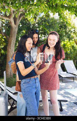 Diverses amies féminines appréciant dans le temps du jardin, souriant et regardant le smartphone ensemble Banque D'Images