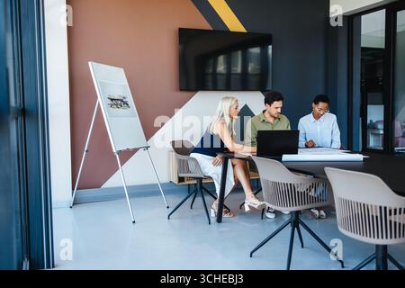 Trois professionnels dans un espace de travail contemporain discutent des documents, favorisant le travail d’équipe et la créativité. Banque D'Images