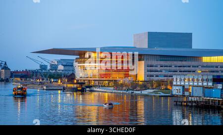 L'Opéra de Copenhague illumine le ciel du soir avec des couleurs vives, reflétant magnifiquement sur l'eau. Les bateaux glissent devant tandis que le paysage urbain offre une superbe toile de fond au Danemark. Banque D'Images