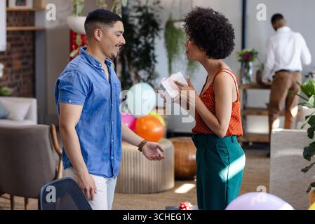 Divers collègues célébrant avec des cadeaux et des ballons dans un cadre de bureau moderne Banque D'Images