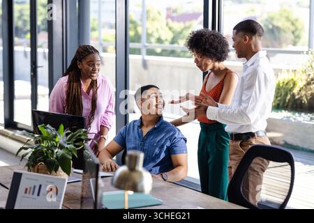 Équipe diversifiée collaborant autour du bureau, discutant du projet avec enthousiasme dans le bureau moderne Banque D'Images