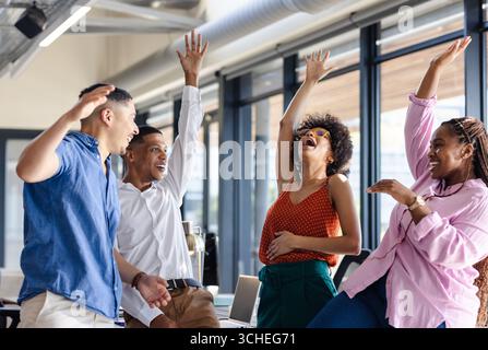 Célébrant le succès, divers collègues lèvent joyeusement la main dans un environnement de bureau moderne Banque D'Images