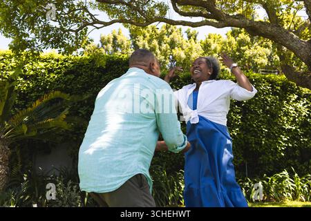 Couple senior profitant d'un moment ludique ensemble dans un jardin luxuriant sous l'arbre Banque D'Images