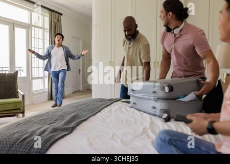 Divers amis masculins déballage des bagages dans la chambre d'amis à la location de vacances, avec des valises grises Banque D'Images