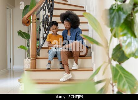 Mère et fils lisant le livre ensemble sur escalier, profitant du temps de qualité Banque D'Images