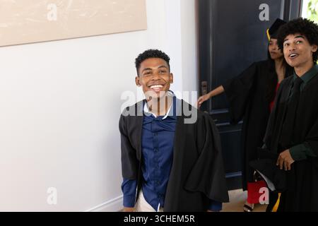Étudiants diplômés en casquettes et robes célébrant avec des expressions joyeuses à la maison Banque D'Images