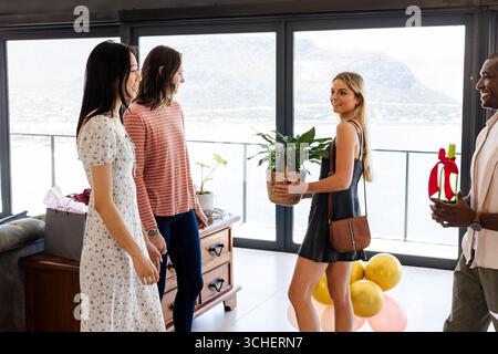 Pendaison de crémaillère, amies diverses célébrant à la maison, échangeant des cadeaux et appréciant le rassemblement joyeux Banque D'Images