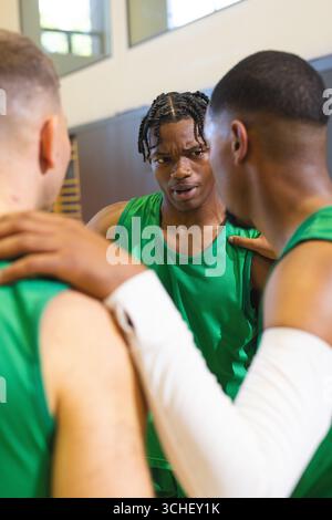 Divers joueurs masculins de basket-ball se blottissant dans la salle de gym portant des maillots verts à côté des barres murales Banque D'Images