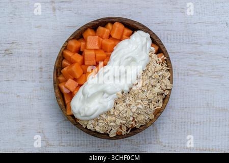Tranches de fruits mûrs de papaye douce avec flocons d'avoine et yaourt blanc sur bol de noix de coco sur fond de bois blanc, gros plan Banque D'Images