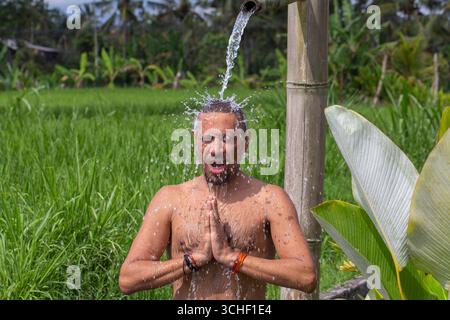 Homme faisant du yoga et méditant en position sous le ruisseau de l'eau sur l'île tropicale Bali, Indonésie. Gros plan. Le concept d'une vie saine Banque D'Images