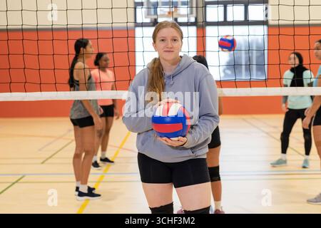 Diverses coéquipières féminines debout derrière le filet de volley-ball sur le gymnase tenant des balles de volley-ball tricolores Banque D'Images