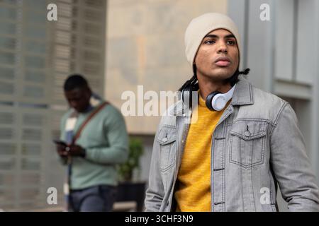 Duo masculin diversifié debout sur la passerelle de la cour près du planteur, portant des écouteurs Banque D'Images