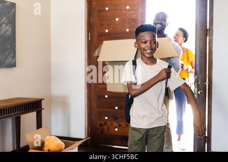 Famille déménageant dans une nouvelle maison, garçon souriant portant un sac à dos, parents tenant des boîtes Banque D'Images