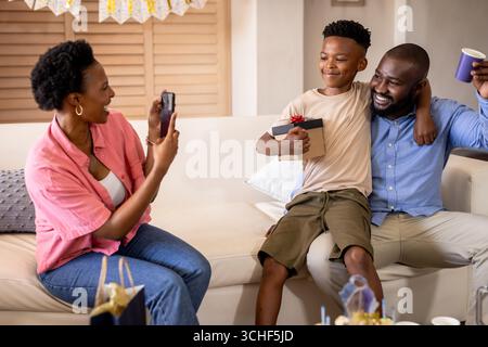 À la fête, famille souriante célébrant l'anniversaire à la maison, capturer des souvenirs avec smartphone Banque D'Images
