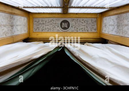 Vue vers le haut de rideaux blancs et verts encadrant un monogramme contre un plafond blanc orné de détails dorés, mettant en valeur la texture luxueuse Banque D'Images