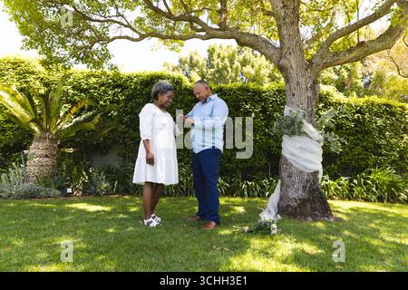Au mariage, échanger des anneaux sous l'arbre, couple senior célébrant un moment spécial dans le jardin Banque D'Images