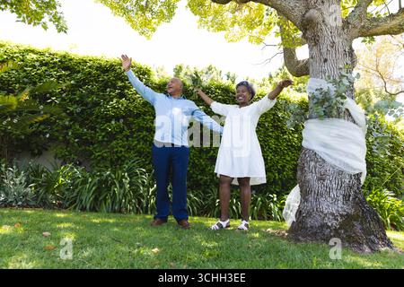 Au mariage, couple Senior embrassant joyeusement la nature sous l'arbre dans un jardin luxuriant Banque D'Images