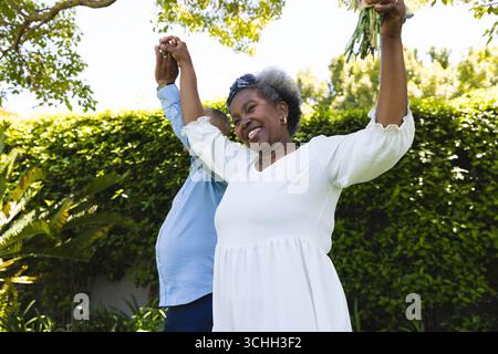 Au mariage, couple Senior dansant joyeusement dans le jardin, se tenant la main et souriant brillamment Banque D'Images