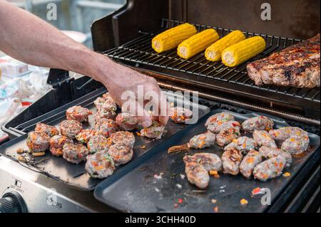 Un gros plan montre une main disposant soigneusement de la viande hachée grillée et du maïs sur le gril. La scène capture l'essence d'un barbecue d'été dans le Banque D'Images