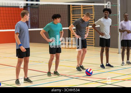 Équipe masculine diversifiée de volley-ball debout sur le terrain avec des lignes de démarcation, filet, volley-ball, baskets Banque D'Images