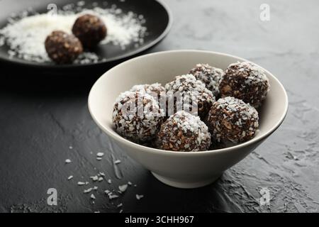 Délicieux bonbons au chocolat avec des noix et des flocons de noix de coco dans un bol sur la table noire, gros plan Banque D'Images