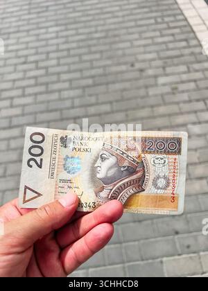Rzeszow, Pologne - 22 août 2025 : gros plan d'une main tenant un billet de banque polonais de 200 zloty contre des carreaux pavés Banque D'Images