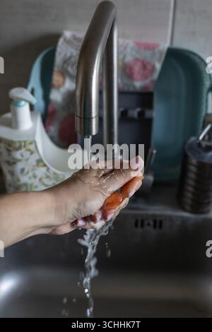 Main féminine essorant une éponge à vaisselle sous l'eau courante sur un évier de cuisine Banque D'Images
