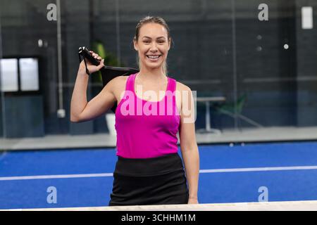 Femme debout sur la cour bleue dans le débardeur rose tenant la raquette à côté de la table avec la plante en pot Banque D'Images