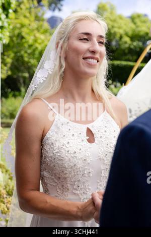 Mariée souriant joyeusement tout en tenant les mains pendant la cérémonie de mariage en plein air Banque D'Images