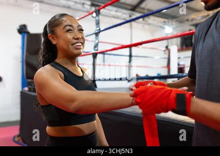 Athlète asiatique et entraîneur debout dans un ring de boxe tout en enveloppant les mains avec des enveloppements rouges, espace de copie Banque D'Images