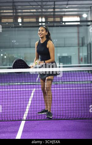 Athlète indienne debout au filet sur le terrain violet en vêtements de sport avec paddle et balle Banque D'Images