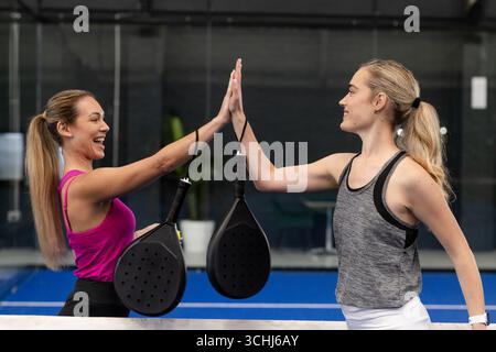 Des amies de sexe féminin en tenue athlétique sur un court de padel et tenant des raquettes noires Banque D'Images